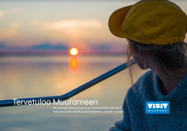 Visit Muurame mainos. Nainen katsoo auringonlaskua järvellä. Tervetuloa Muurameen -teksti