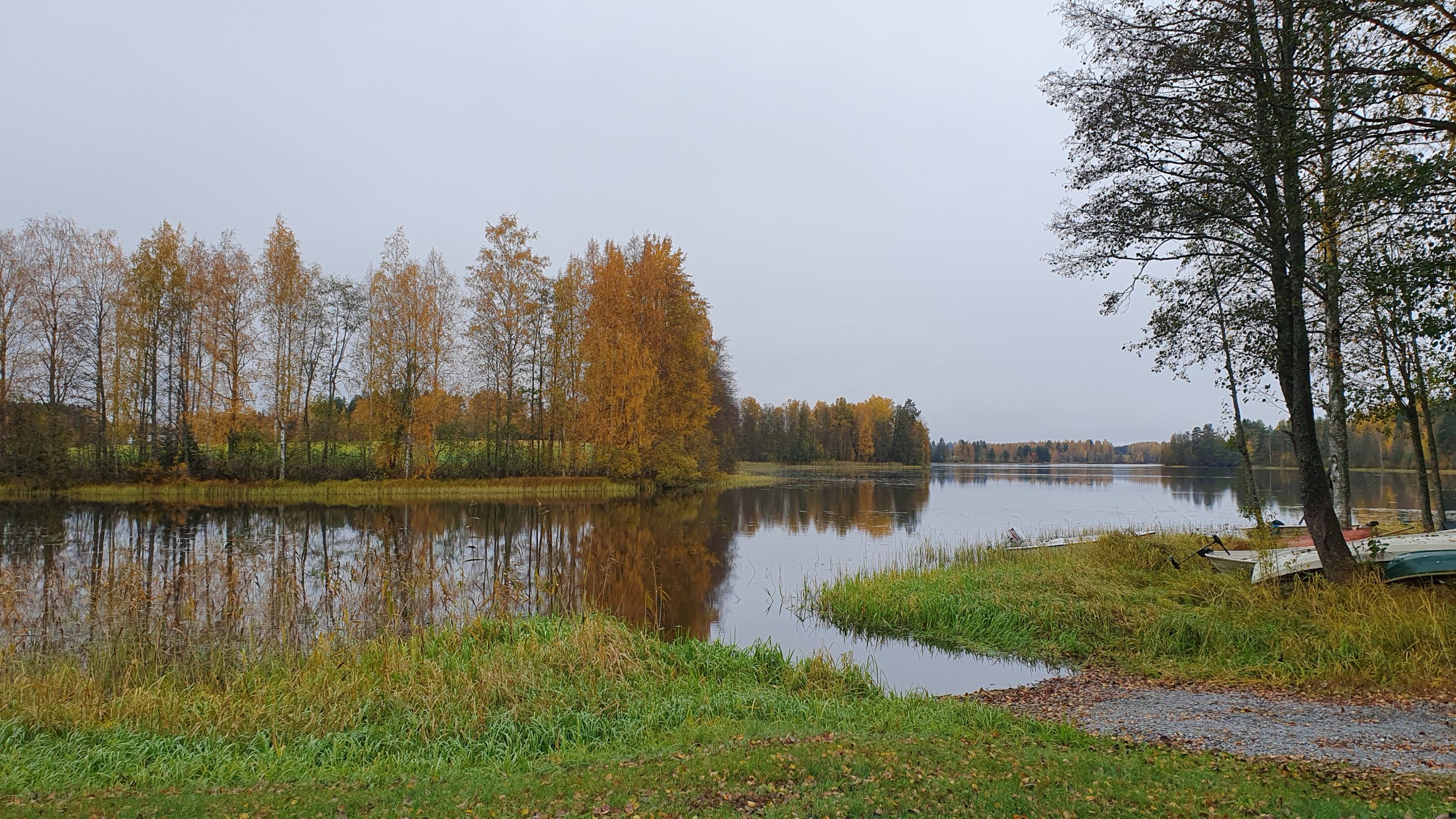 Järvi, joka kapenee salmeksi kuvan vasemmassa reunassa. Vastarannalla lehtipuita ruskassa, osasta jo pudonnut lehdet. Oikeassa reunassa on muutama soutuvene rannalla.