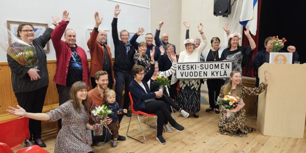 Parikymmentä Havusalmen kyläläistä poseeraa kädet ylhäällä ja iloisina Keski-Suomen Vuoden Kylän valinnasta.