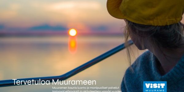 Visit Muurame mainos. Nainen katsoo auringonlaskua järvellä. Tervetuloa Muurameen -teksti